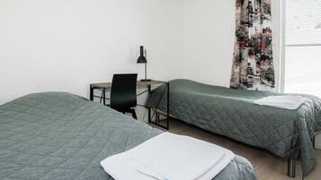 A room with two beds, a desk, a chair, and a window with curtains.
