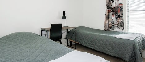 Una habitación con dos camas, un escritorio, una silla y un ventanal con cortinas.