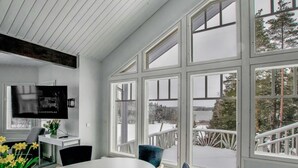 Una habitación moderna con un ventanal grande, un televisor de pantalla plana, una mesa de comedor y una silla.