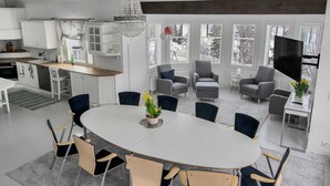 Una cocina moderna con armarios blancos, un comedor con mesa y sillas redondas, y una sala de estar con sofás grises y un televisor.