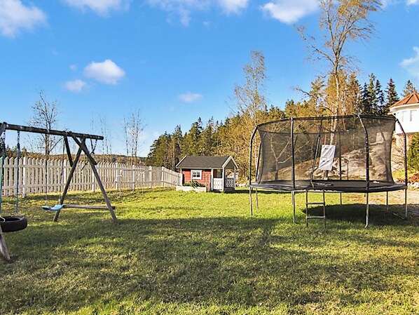 Un patio trasero con un columpio, un trampolín, una valla de madera y una casita.