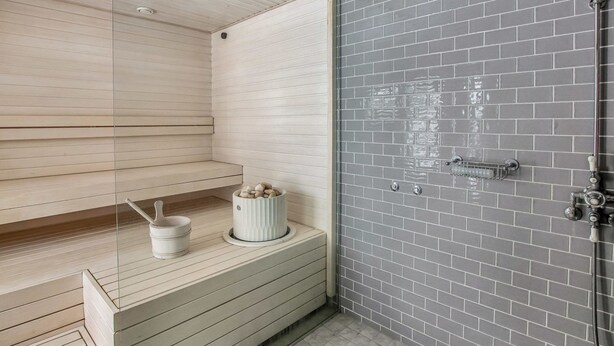 Un baño moderno con un banco de madera, un pequeño recipiente blanco y una zona de ducha con pared de azulejos grises.
