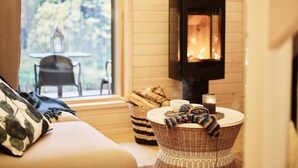 Una habitación acogedora con chimenea, un sofá, una cesta de mimbre y vistas al exterior.