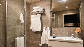 Une salle de bain moderne avec une douche à parois de verre, des toilettes, un lavabo agrémenté d’un vase de fleurs et un porte-serviettes avec des serviettes pliées.