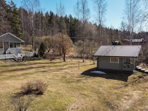 A small house with a porch and a fenced yard, surrounded by trees and a hill.