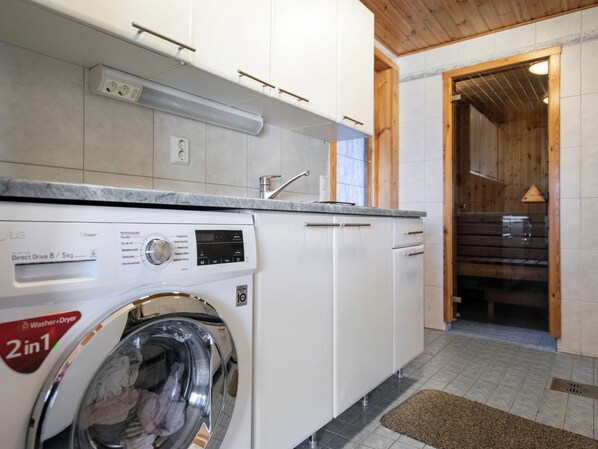 A compact kitchen with a built-in washer and dryer, white cabinets, and a wooden ceiling.