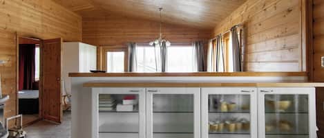 Un intérieur en bois avec un espace cuisine comprenant un îlot central doté de placards et d’un réfrigérateur.