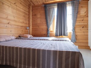 A wooden cabin room with two beds, a window with curtains, and a wall-mounted light. - Ketunkolo by Interhome (Tampere)