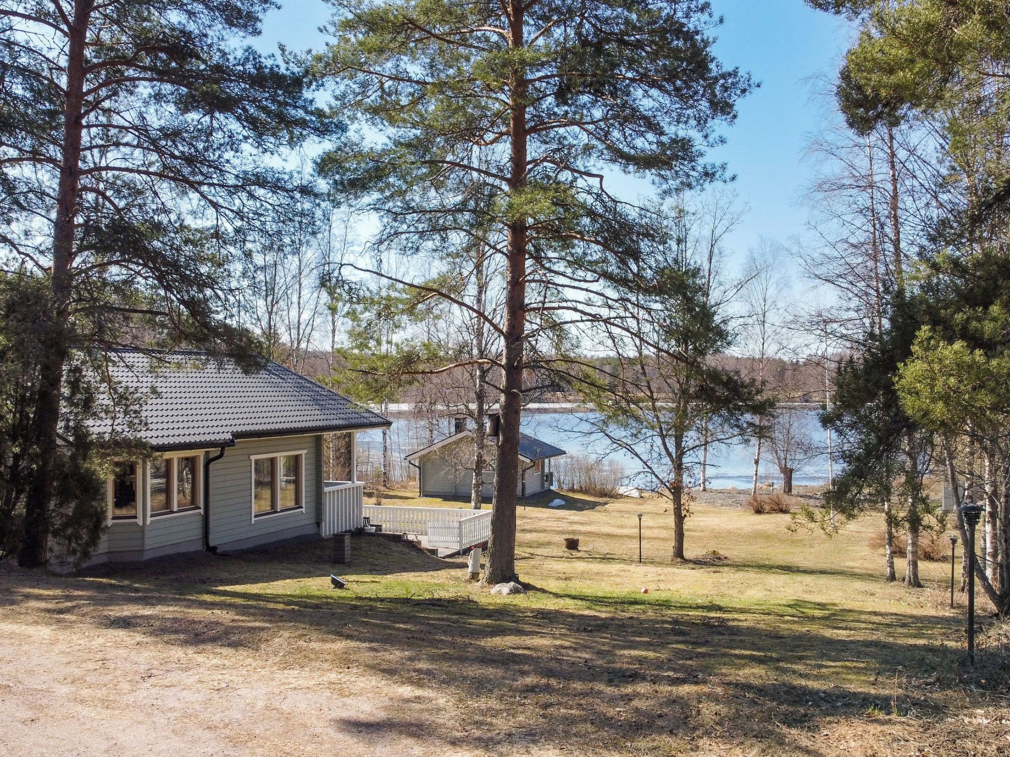 A cabin with a porch and a small deck, surrounded by trees and a lake.