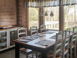 A wooden interior with a dining table set for six, chairs, a kitchen area, and a view of trees through large windows. - Ketunkolo by Interhome (Tampere)