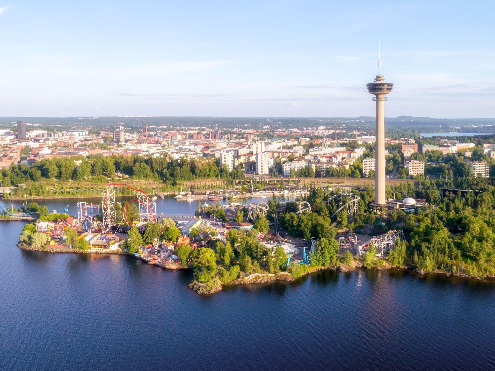 Une vue aérienne d’une ville avec une tour imposante, une rivière et un parc avec des manèges.