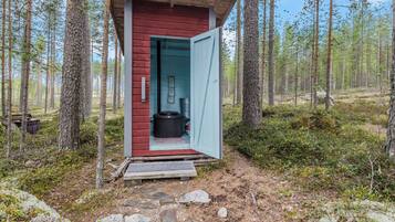 A small cabin with a red exterior and a blue door, surrounded by a forest.