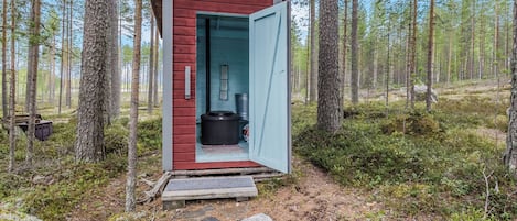 A small cabin with a red exterior and a blue door, surrounded by a forest.