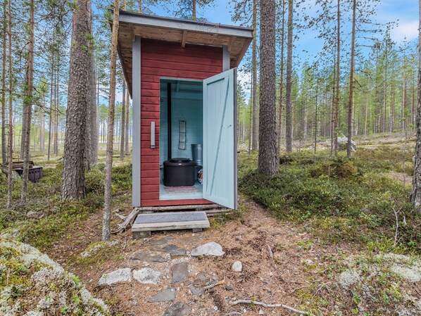 A small cabin with a red exterior and a blue door, surrounded by a forest.