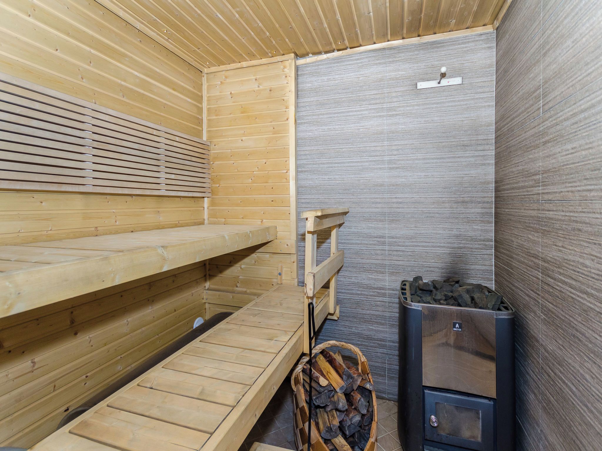 Een sauna met houten banken, een bank met rugleuning, een wandheater en een prullenbak.