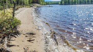 Une plage de sable avec une jetée en bois qui s’avance sur un lac paisible, le tout entouré d’une forêt dense.