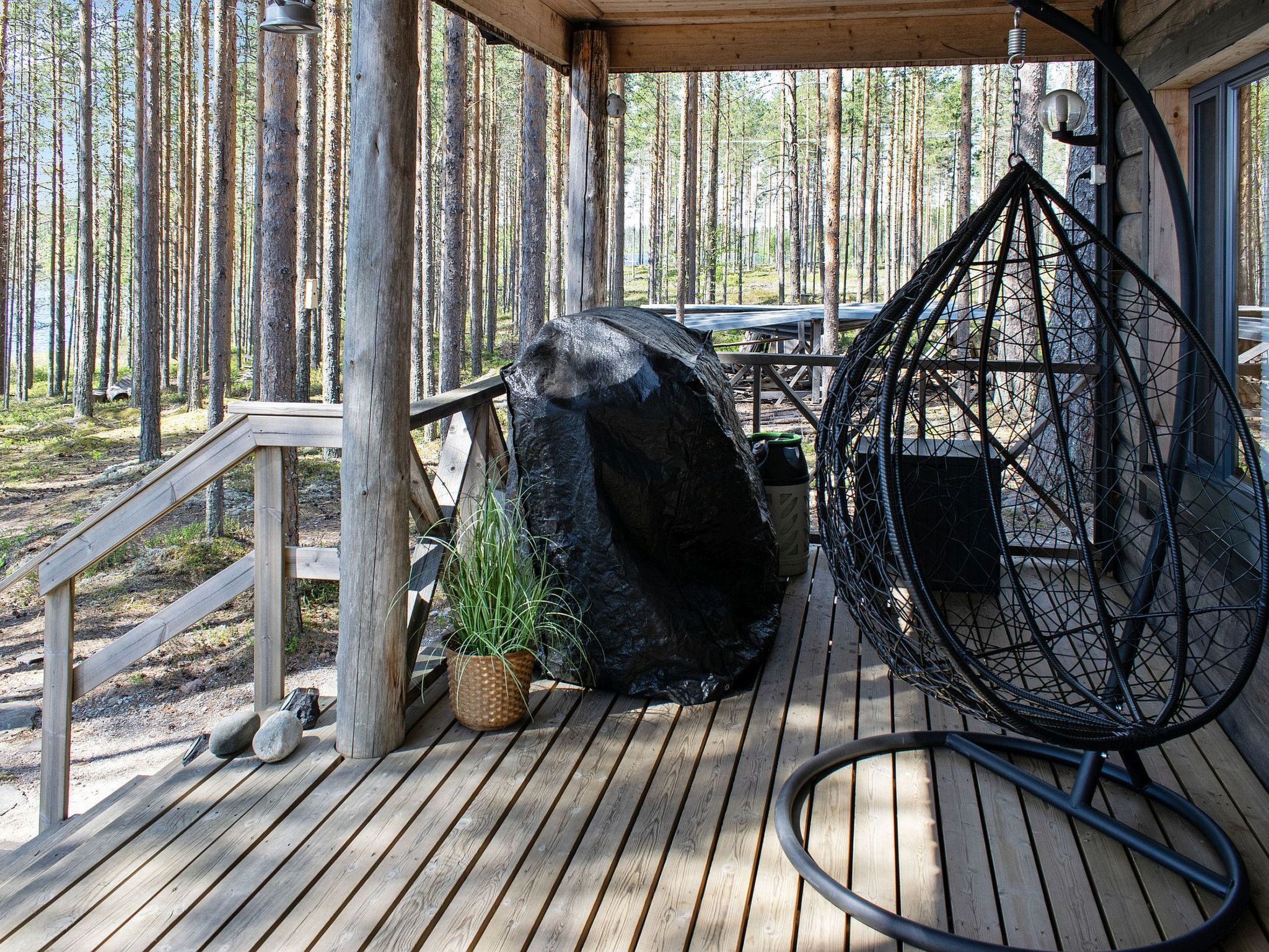 A wooden deck with a hanging chair, a large rock, and a potted plant.