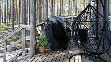 A wooden deck with a hanging chair, a large rock, and a potted plant.