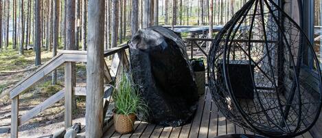 Une terrasse en bois avec un fauteuil suspendu, un grand rocher et une plante en pot.