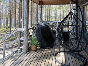A wooden deck with a hanging chair, a large rock, and a potted plant.