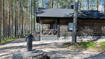 A wooden cabin with a porch, surrounded by a forest.