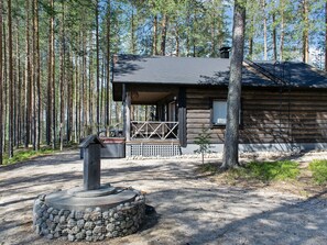 A wooden cabin with a porch, surrounded by a forest.