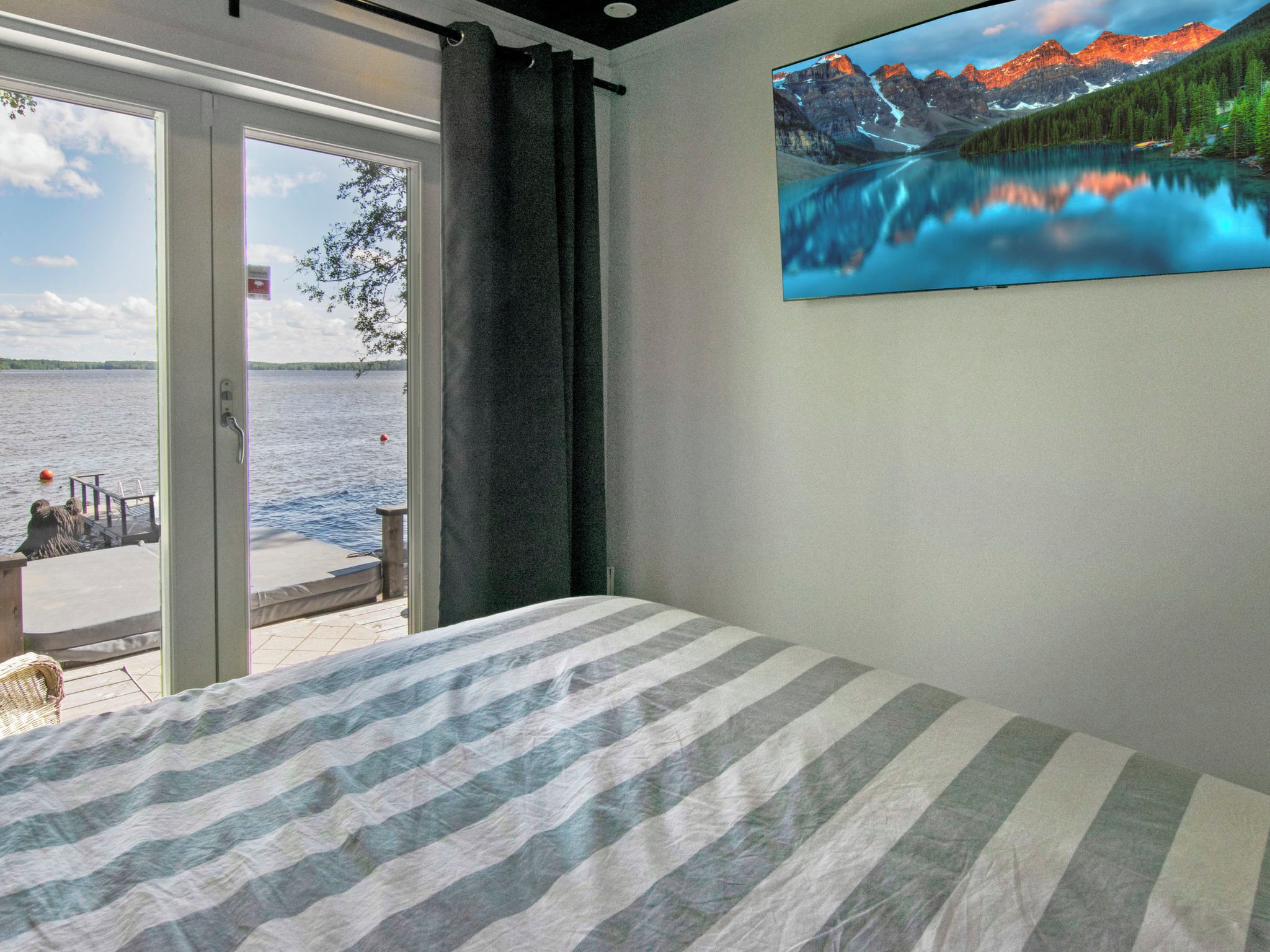 A bedroom with a bed, a window with a view of a lake and mountains, and a painting of a mountain landscape.