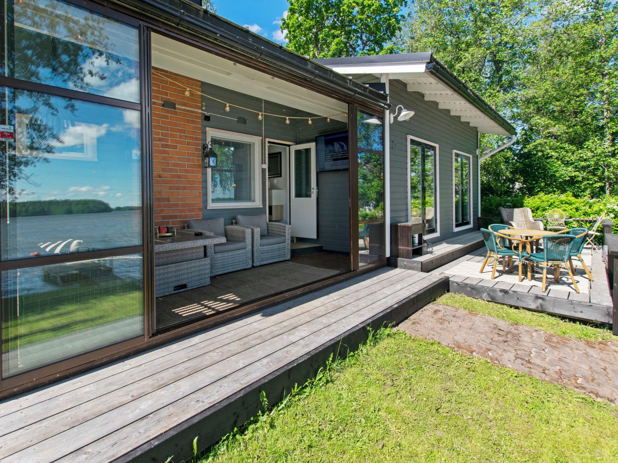 Una casa moderna con un'ampia vetrata, un terrazzo in legno e mobili da esterno.