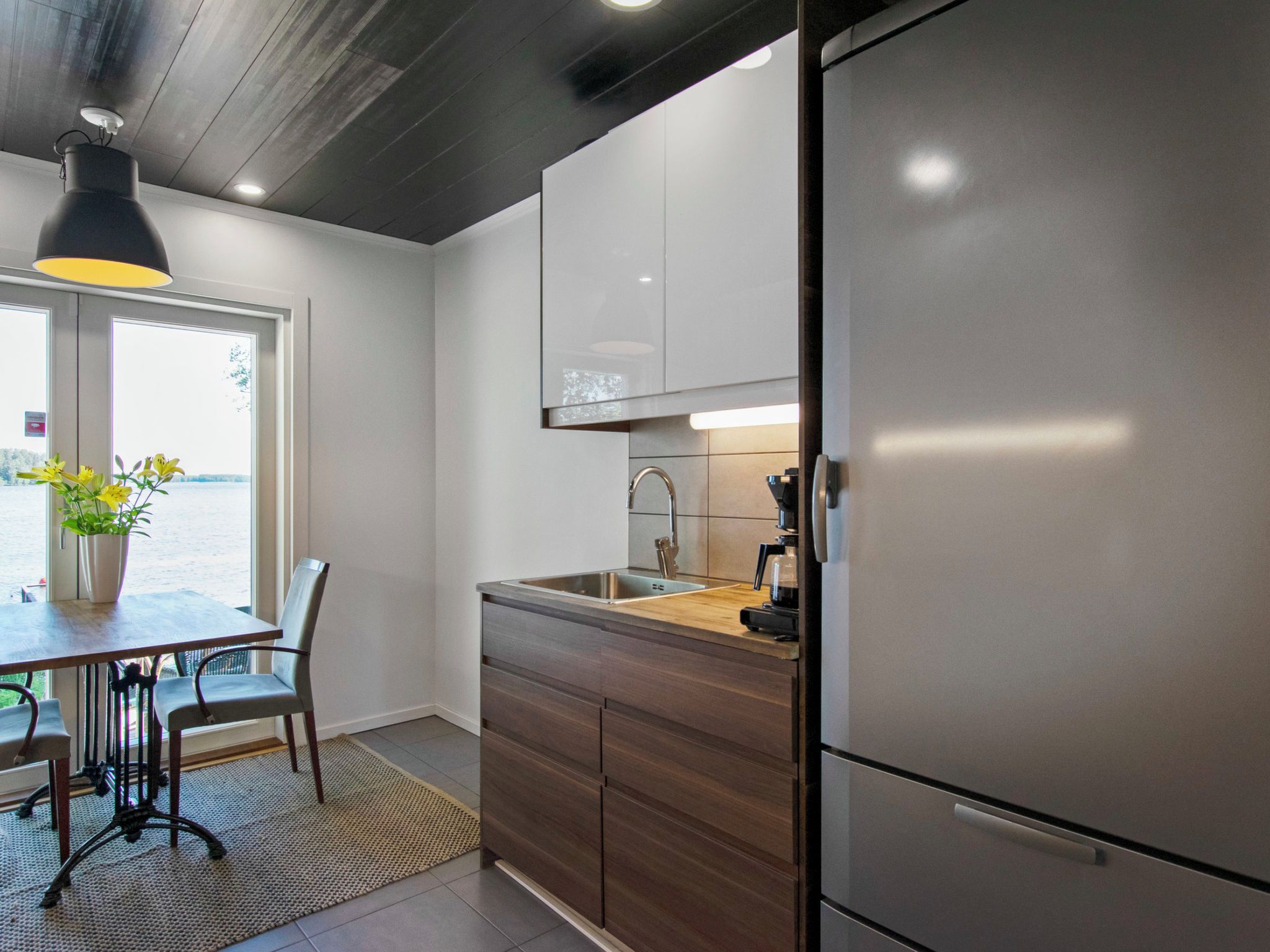 Una cucina moderna con frigorifero in acciaio inox, pensili in legno, un lavello e un'area pranzo con tavolo e sedie.