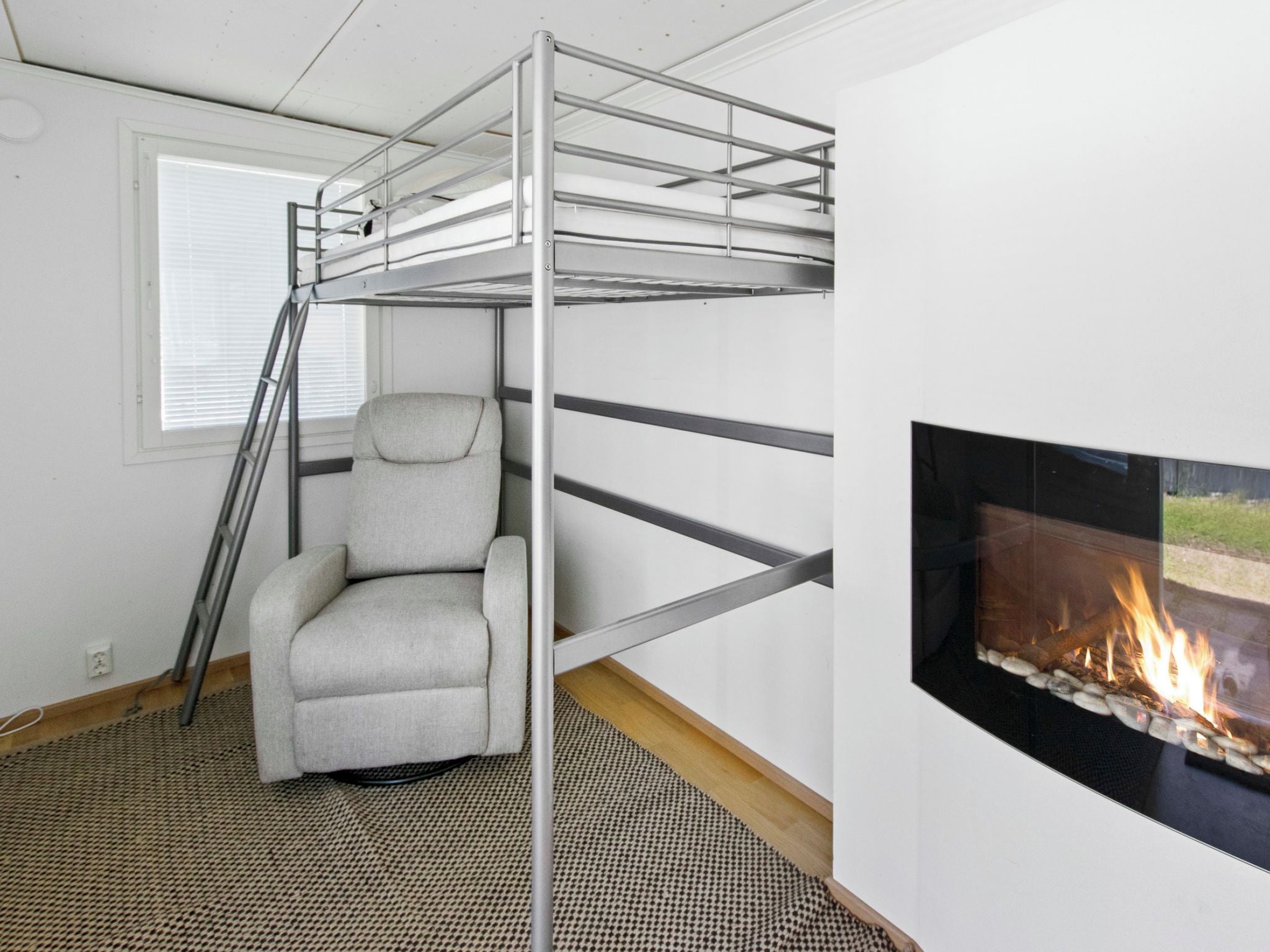 A bunk bed with a ladder, a chair, and a fireplace in a room with a window and a patterned rug.