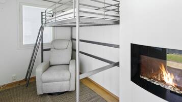 A bunk bed with a ladder, a chair, and a fireplace in a room with a window and a patterned rug.