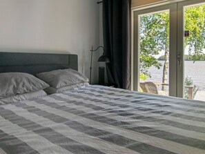 A bedroom with a bed, a nightstand, a lamp, and a view of a lake through a sliding door.