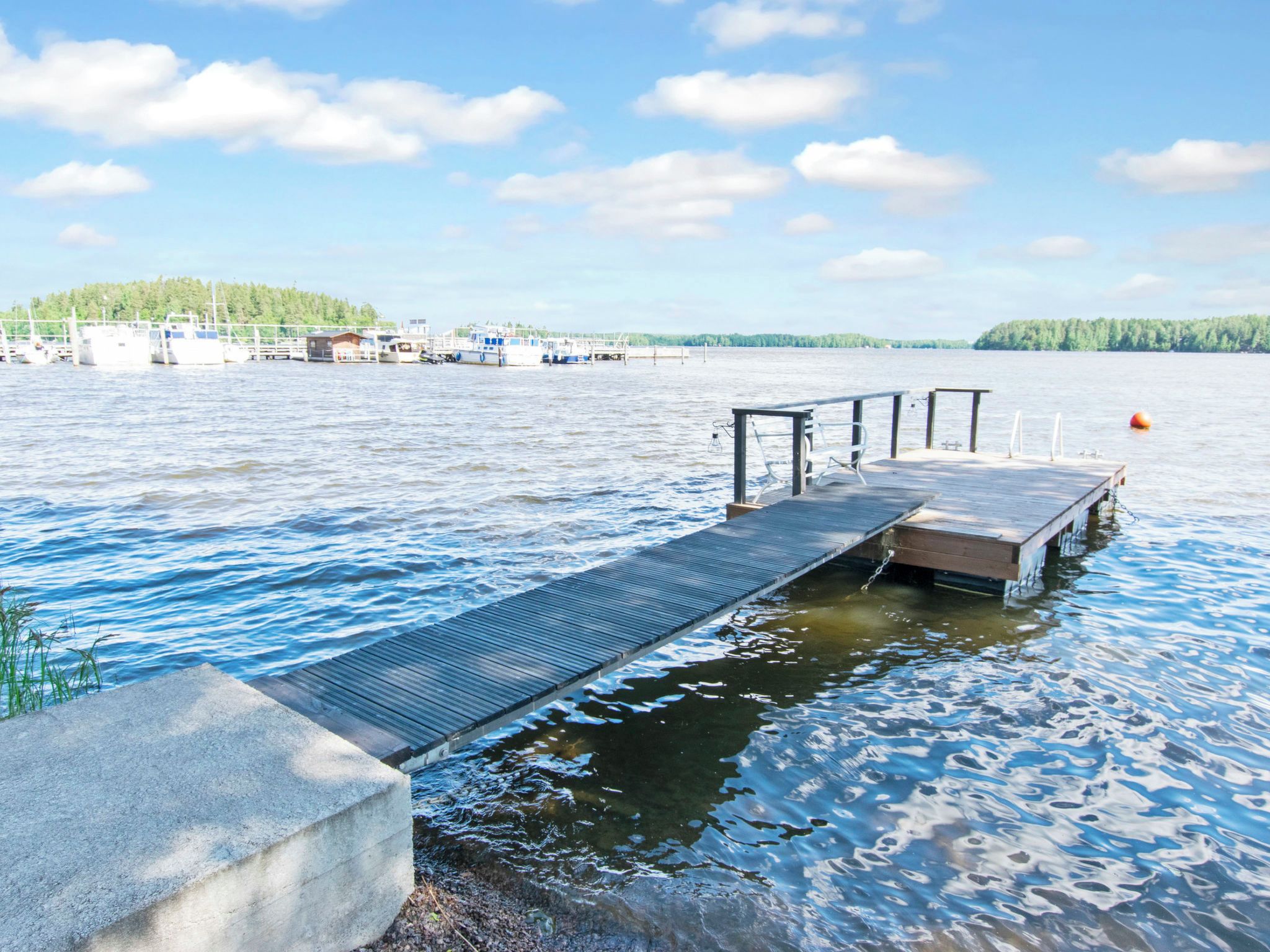 A wooden dock extending into a calm lake with boats docked in the background.