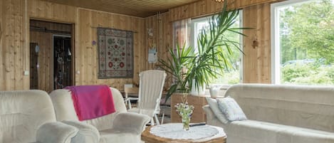 Et hyggeligt værelse med trævægge, en lysekrone, en sofa, en stol og et bord med en blomstervase.