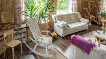 Uma sala de estar aconchegante com uma cadeira de balanço, um sofá e uma mesa de centro. Há uma planta grande e um lustre.