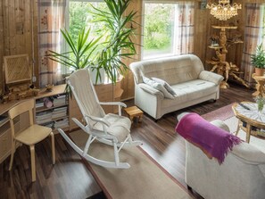 A cozy living room with a rocking chair, a sofa, and a coffee table. There is a large plant and a chandelier.