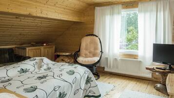 A cozy room with a bed, a chair, a desk with a computer, and a window with curtains.