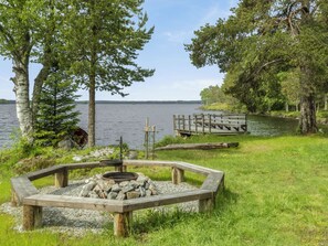 A lakeside campsite with a fire pit, a wooden deck, and a dock extending into the water. - Vacation home Käpylä by Interhome (Kuhmo)