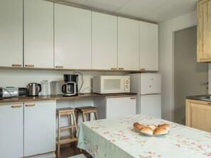 A compact kitchen with white cabinets, a microwave, a coffee maker, and a table with bread.
