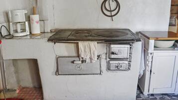 Uma cozinha com fogão, cafeteira e vassoura.