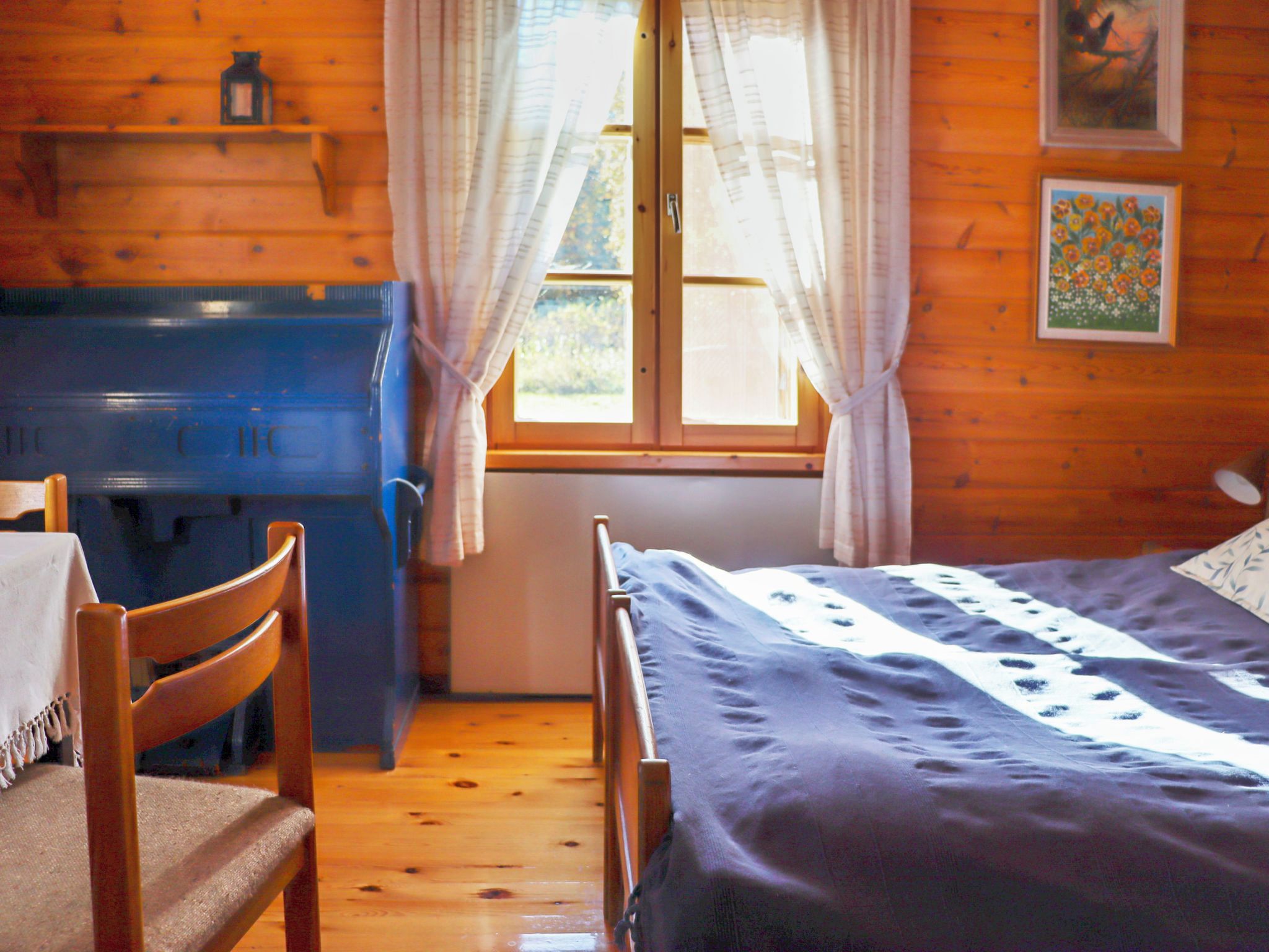 Una habitación con cama, escritorio, silla, ventana con cortinas y un cuadro en la pared.