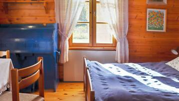 Una habitación con cama, escritorio, silla, ventana con cortinas y un cuadro en la pared.
