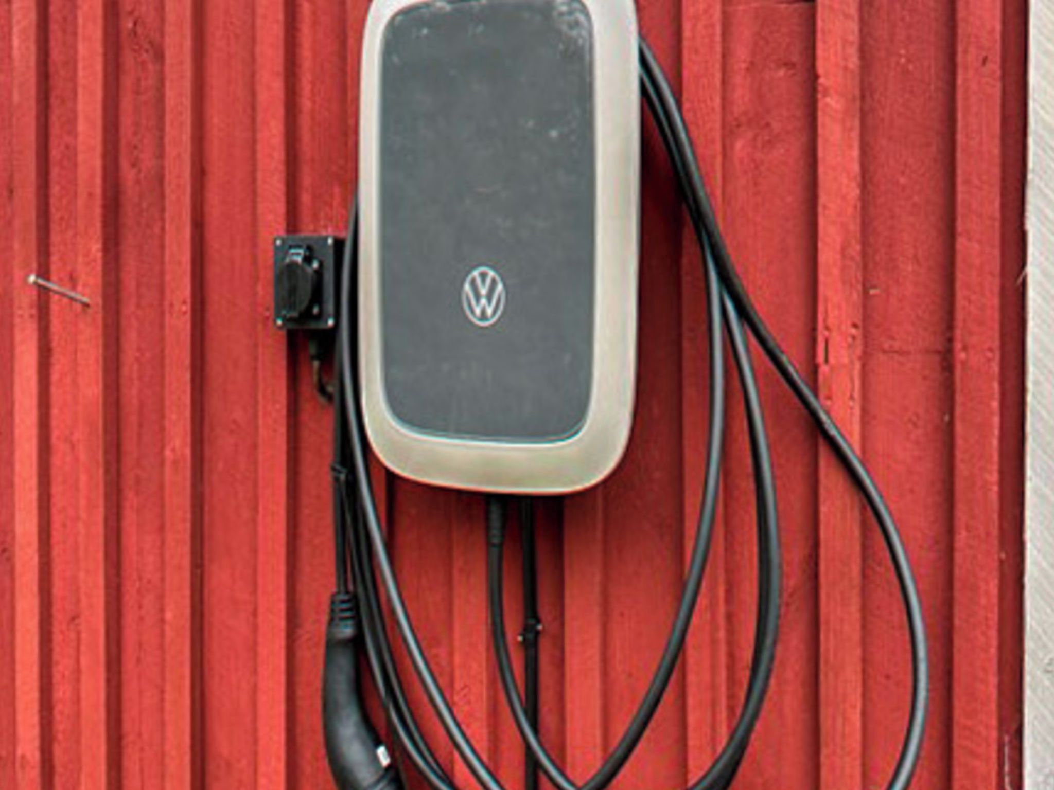 Una estación de carga con el logotipo de Volkswagen, conectada a una pared roja.
