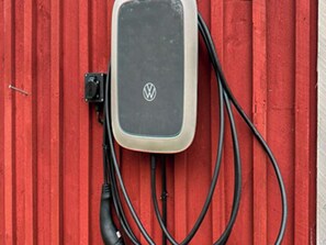 Une borne de recharge ornée du logo Volkswagen, fixée à un mur rouge.