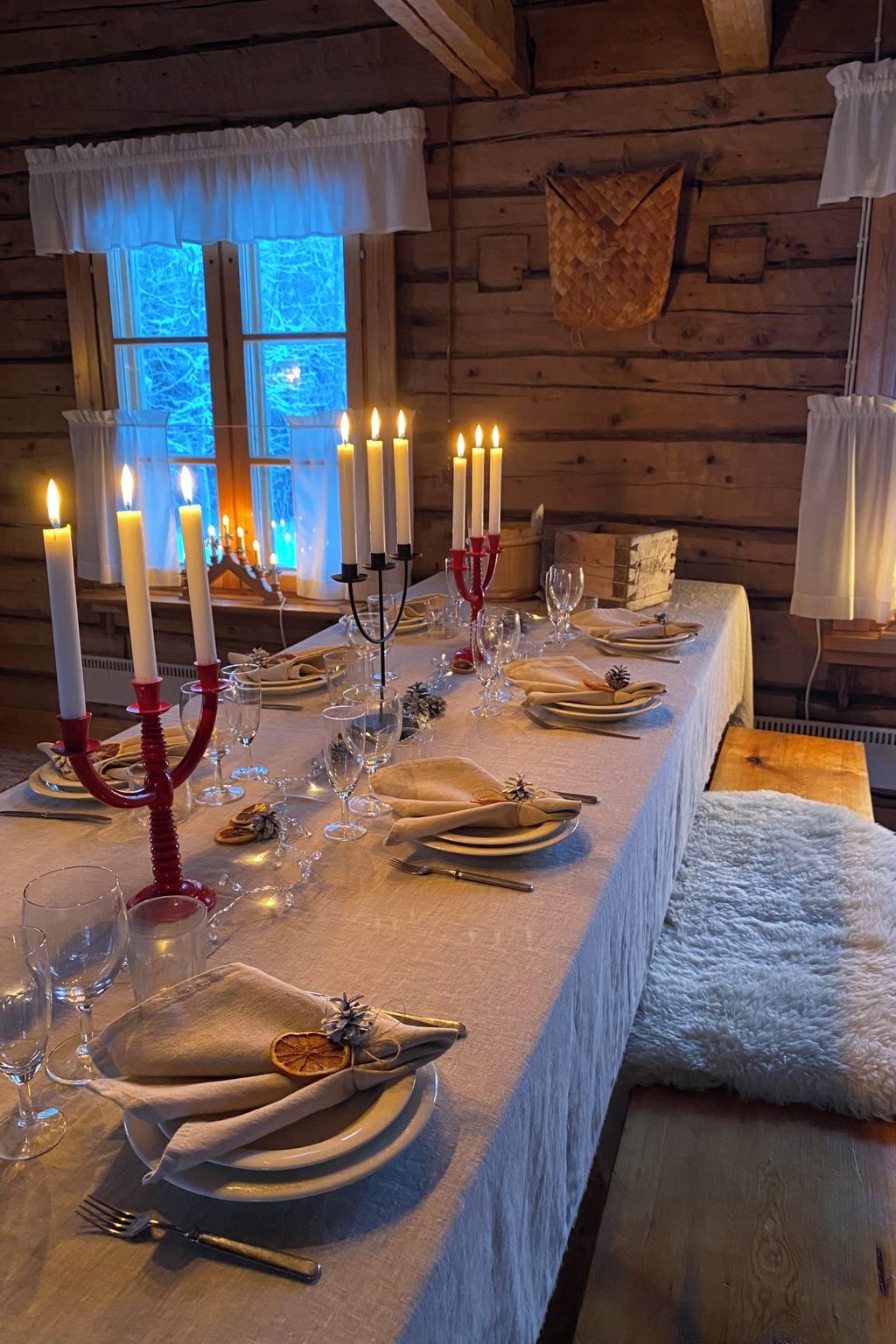 Ein langer Esstisch, gedeckt für eine Mahlzeit, mit Kerzen, Gläsern und Tellern.