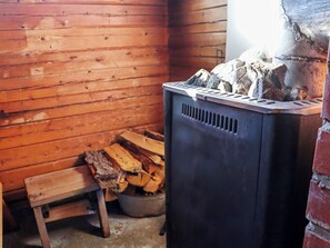 Una estufa de leña con troncos y un pequeño banco en una cabaña de madera.