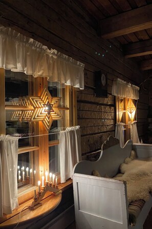 A cozy cabin interior with a wooden ceiling, a bed with a fur throw, and a window with a star-shaped light fixture.