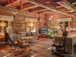 A cozy log cabin interior with a wooden ceiling, a Christmas tree, and a television.
