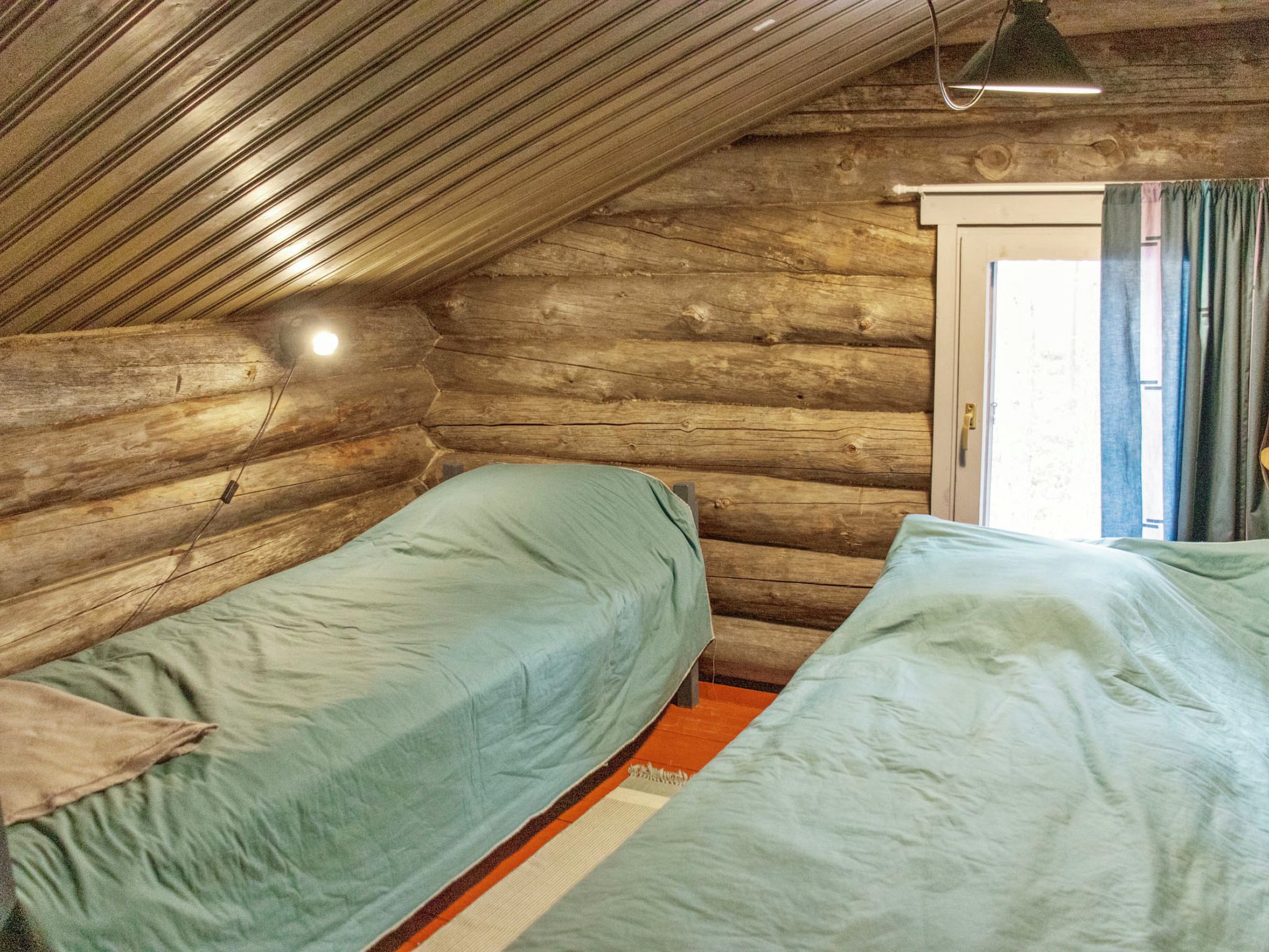 Una cabaña con dos camas, techo inclinado y ventana con cortinas.
