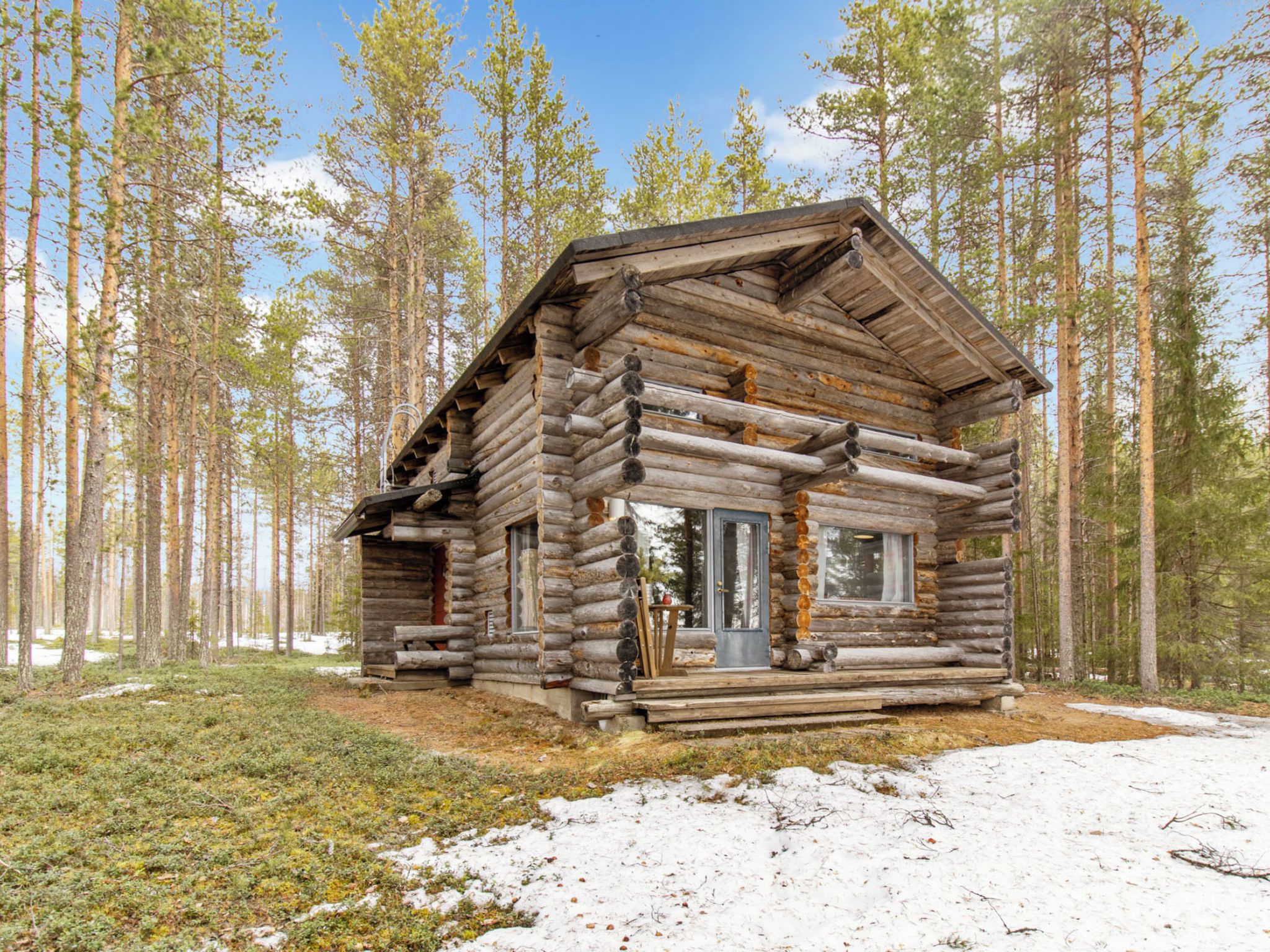 Une cabane en rondins avec un porche à l’avant, entourée d’une forêt.
